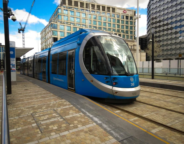 a blue and white train traveling down train tracks, coventry city centre, street tram, avatar image, futuristic marrakech