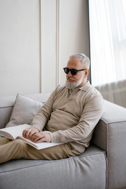 a man sitting on a couch reading a book, implanted sunglasses, dark grey haired man, mental health, 2019 trending photo