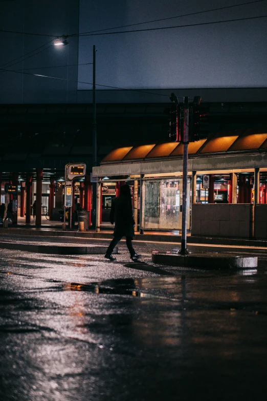 a person walking across a wet street at night, by Tobias Stimmer, unsplash contest winner, bus station, north melbourne street, taverns nighttime lifestyle, moody morning light