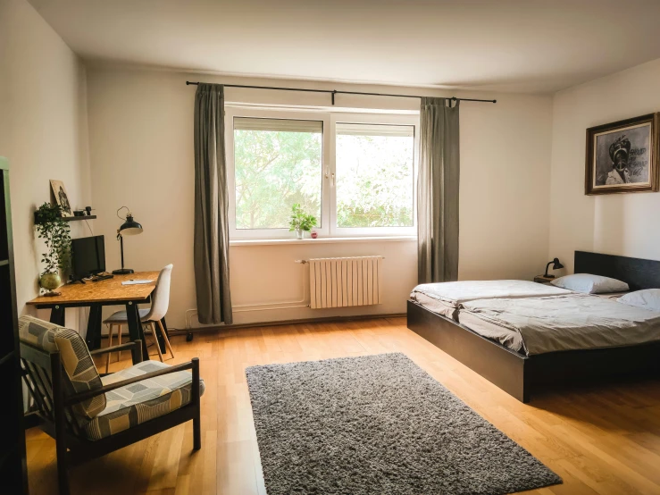 a bedroom with two beds, desk, chairs, lamp, and window