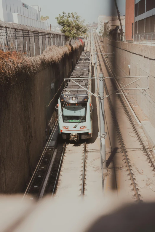 a train traveling down train tracks next to a tall building, camera looking down upon, high walled tunnel, 🚿🗝📝