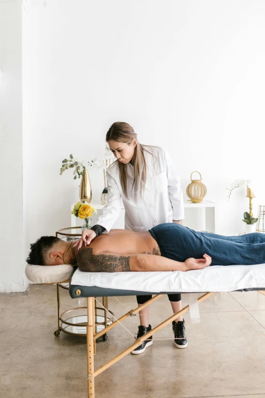 a man laying on a massage table next to a woman, a photo, by Gavin Hamilton, trending on unsplash, in a white boho style studio, gold line tattoos, inspect in inventory image, asian male