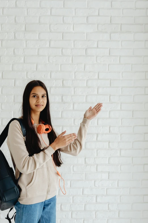 a woman standing in front of a white brick wall, trending on pexels, in a school classroom, pointing, with a backpack, young woman with long dark hair