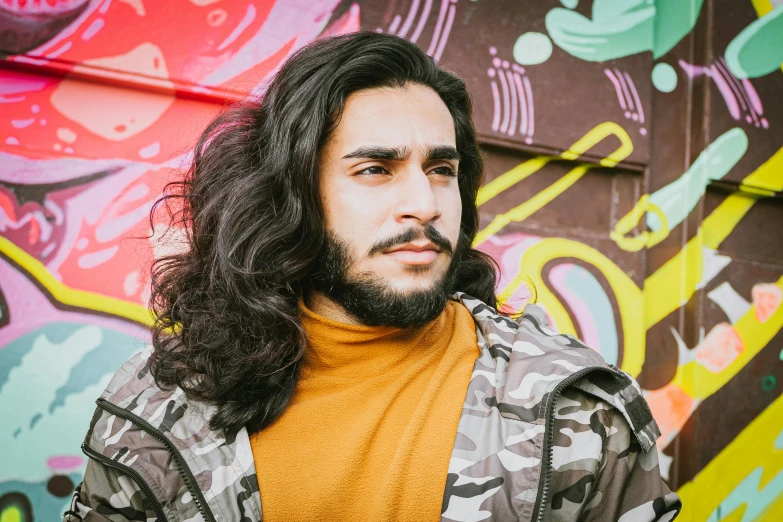 a man with long hair standing in front of a graffiti wall, trending on pexels, arab man light beard, charli bowater and artgeem, headshot profile picture, long curly black hair