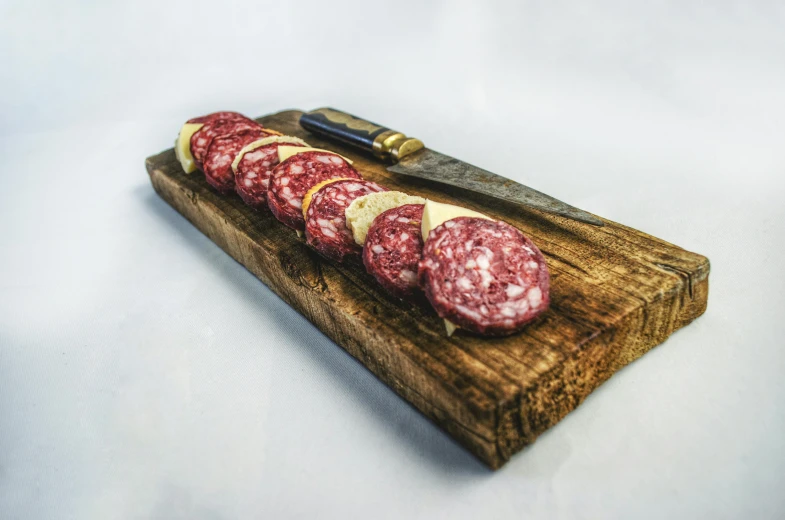 sliced sausage on a cutting board with a knife, by Tom Wänerstrand, pexels, cheesy, crimson themed, on a wooden tray, long shot wide shot full shot