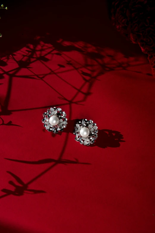 a pair of earrings sitting on top of a table, inspired by Antoni Brodowski, unsplash, baroque, on a red background, jingna zhang, pearl silverplate, sparkling petals