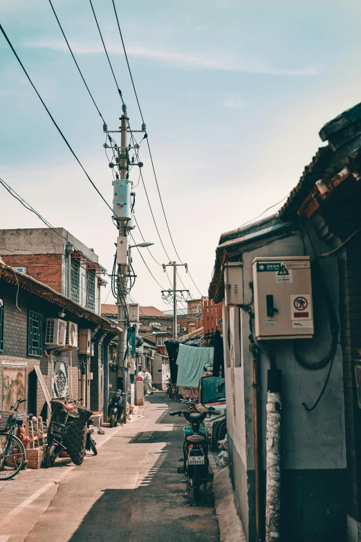 a couple of bikes parked on the side of a road, by Jang Seung-eop, pexels contest winner, mingei, houses on stilts, cables everywhere, back alley, in the middle of a small colony