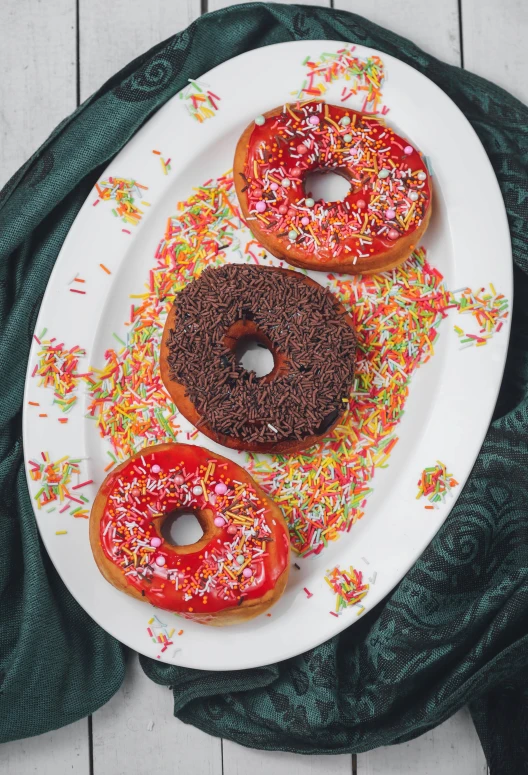 a white plate topped with three donuts covered in sprinkles, a colorized photo, inspired by david rubín, unsplash, red and brown color scheme, malaysian, chocolate river, lush and colorful eclipse