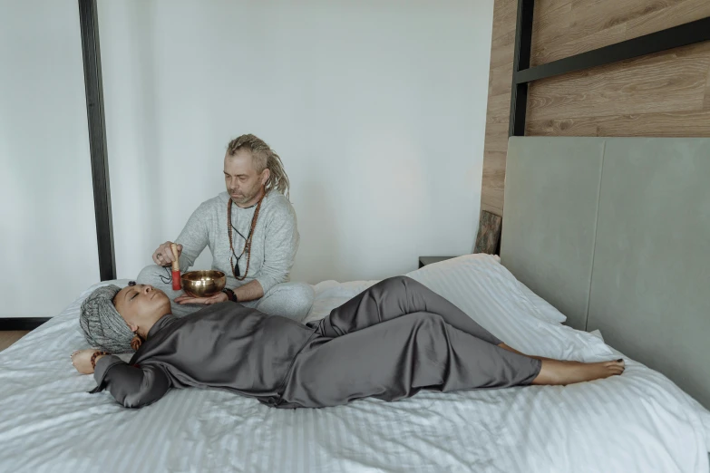 a woman laying on top of a bed next to a man, by Jan Tengnagel, pexels contest winner, hurufiyya, monk's robe, healing pods, grey, full body image