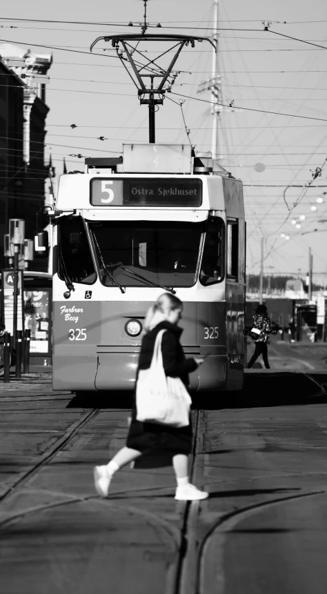 a black and white photo of a woman crossing a street, a black and white photo, street tram, fine!!! lines, toronto city, helsinki