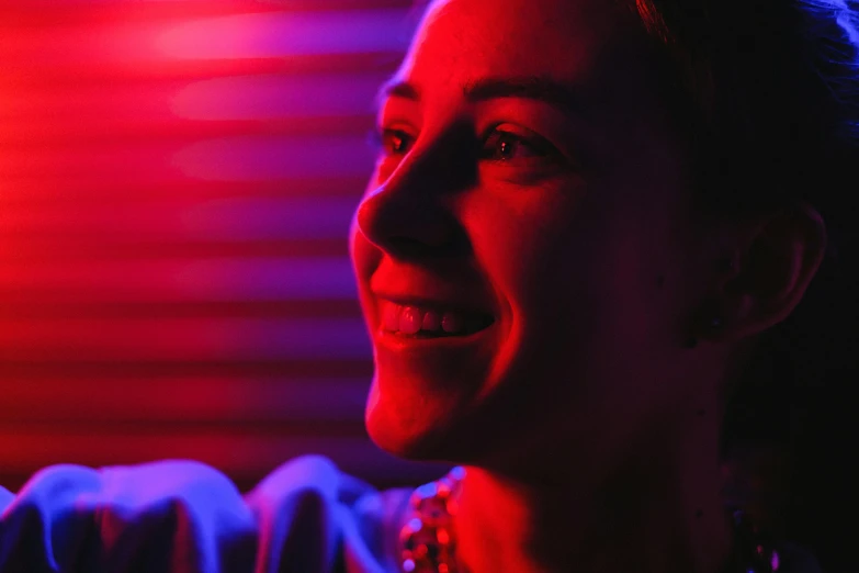 a woman smiling in front of a red light, pexels contest winner, digital art, purple ambient light, red and blue black light, cinematic closeup, volumetric lighting. red