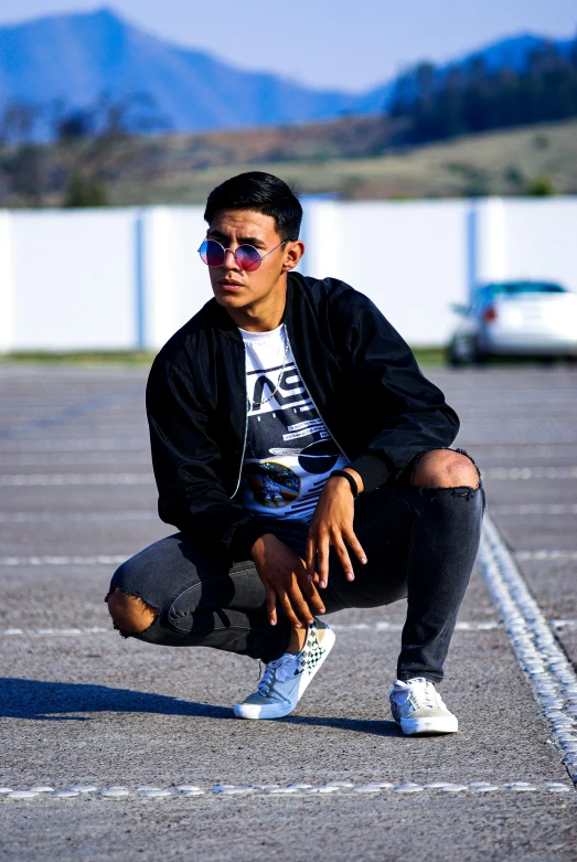 a man kneeling in a parking lot wearing his sunglasses