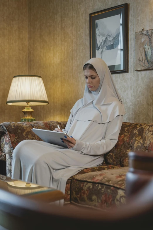 a woman sitting on a couch in a living room, trending on reddit, renaissance, white hijab, nun outfit, hotel room, ( ( theatrical ) )