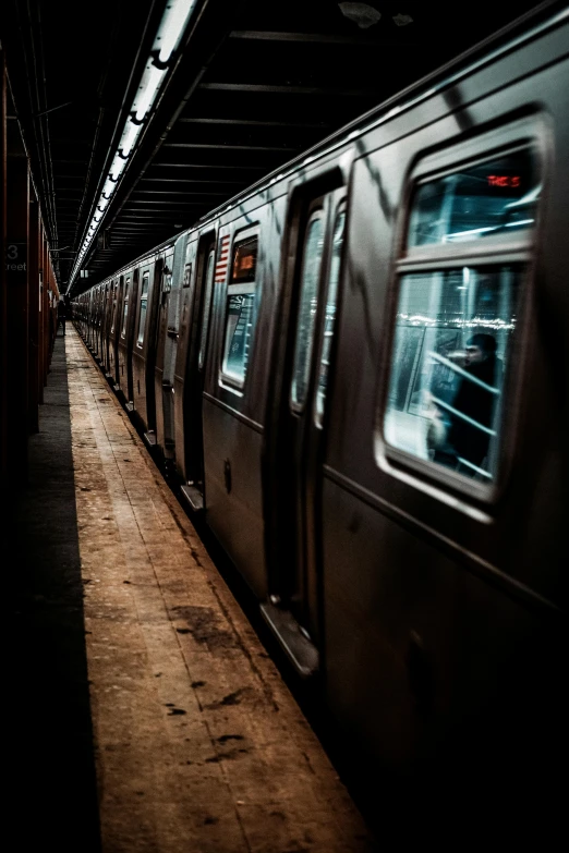 a subway train pulling into a station next to a platform, by Matt Stewart, unsplash contest winner, dark. no text, in the middle of new york, rows of windows lit internally, 🚿🗝📝
