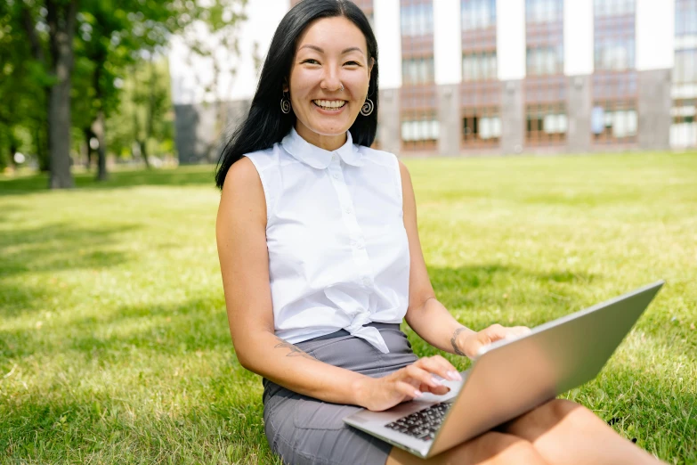 a woman sitting in the grass with a laptop, leslie zhang, wearing business casual dress, russian academic, at college