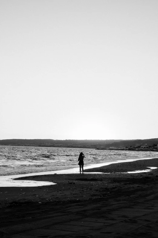 a person standing on a beach next to the ocean, a black and white photo, by Altichiero, contre - jour, red sea, “ femme on a galactic shore, notan
