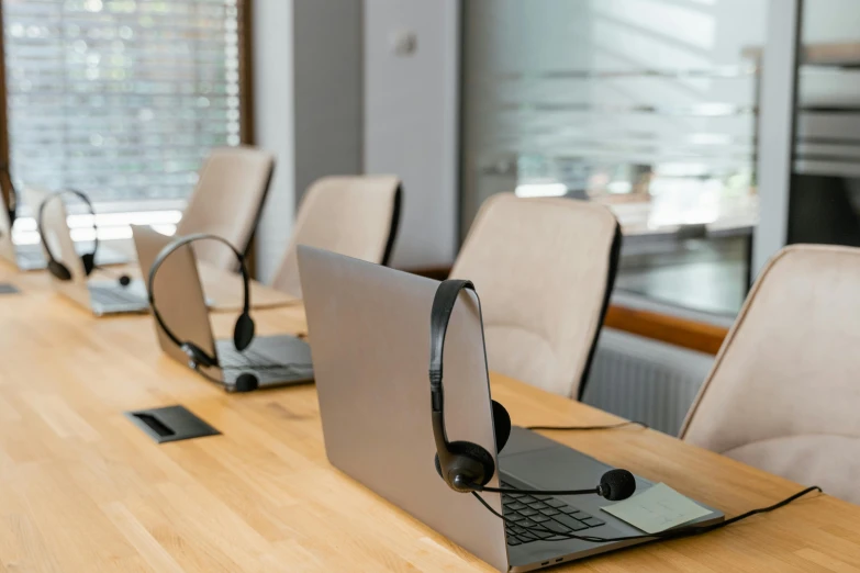 a row of laptops sitting on top of a wooden table, trending on pexels, hurufiyya, in an call centre office, avatar image, headset, royal commission