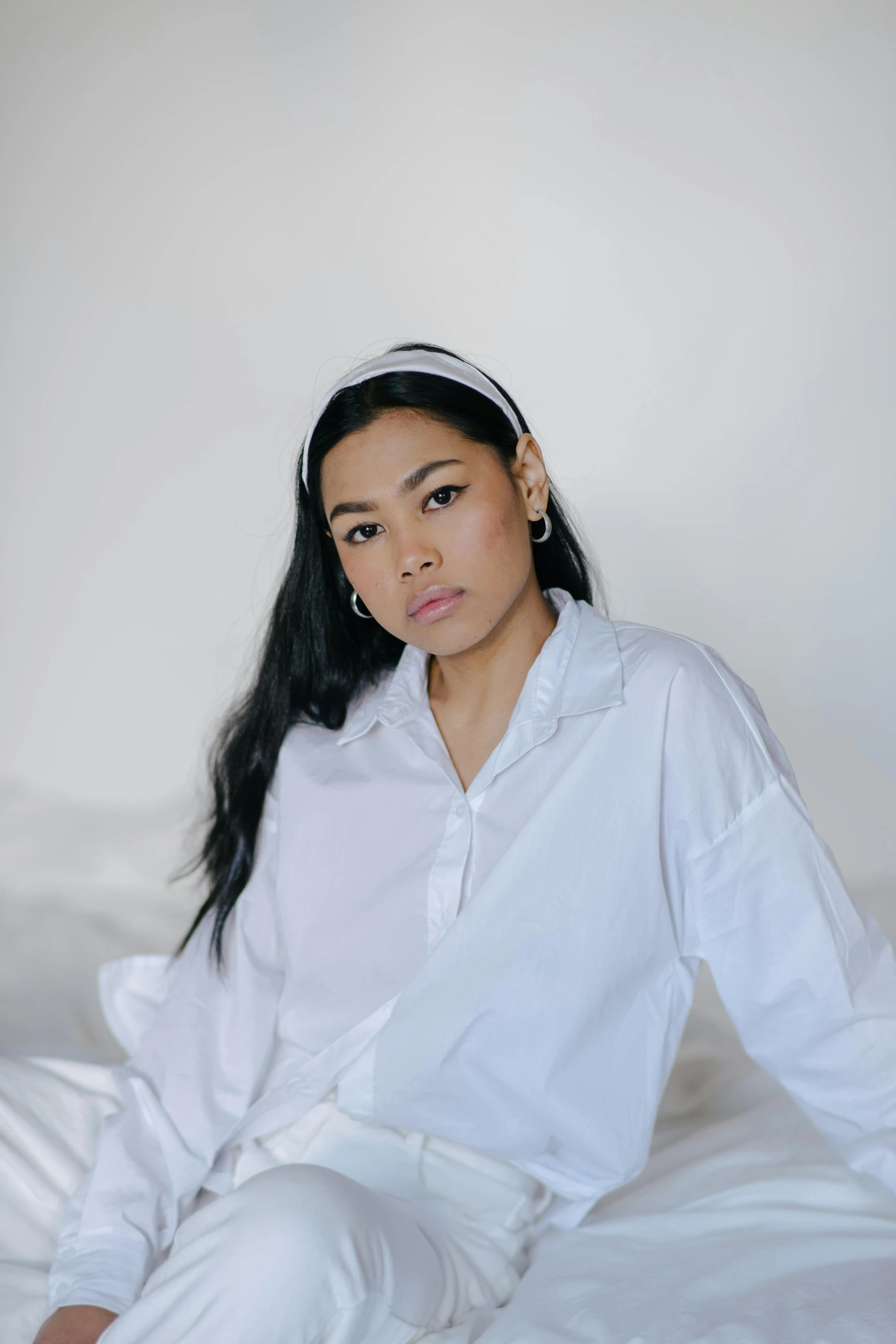 a woman sitting on a bed wearing a white shirt and pants, an album cover, inspired by Ruth Jên, trending on pexels, wearing a headband, wearing a white button up shirt, headshot, light skin