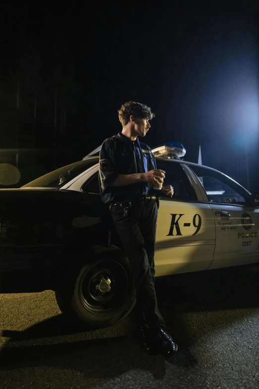 a man standing beside a police car in the dark