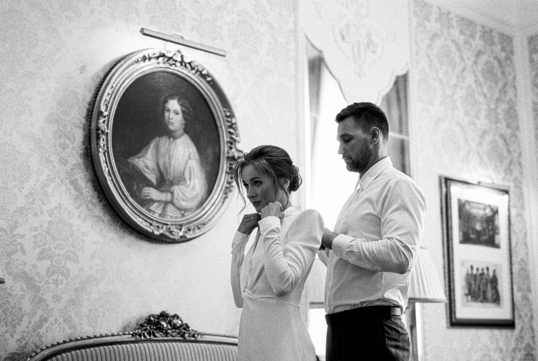 a man helping a woman fix her tie, a black and white photo, by Emma Andijewska, romanticism, decoration around the room, dmitry prozorov style, white dress shirt, gif