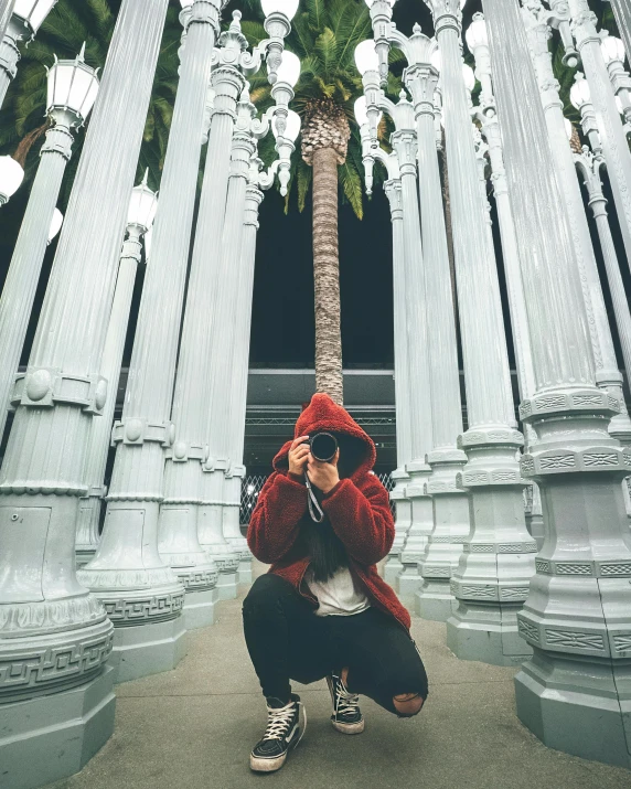 a person squatting in front of a palm tree, a statue, unsplash contest winner, visual art, wearing a red hoodie, tall columns, hollywood, lgbtq