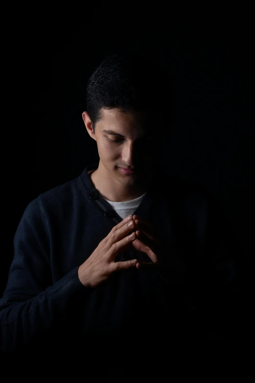 a man standing in the dark with his hands on his chest, an album cover, inspired by Alexis Grimou, unsplash, male teenager, gestures, headshot profile picture, doing a prayer