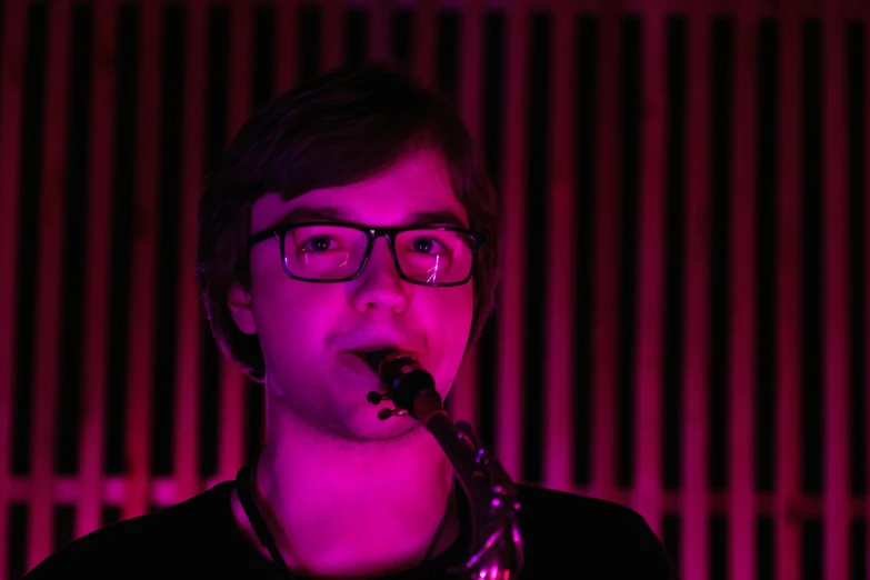 man wearing glasses with microphone in front of bright pink light