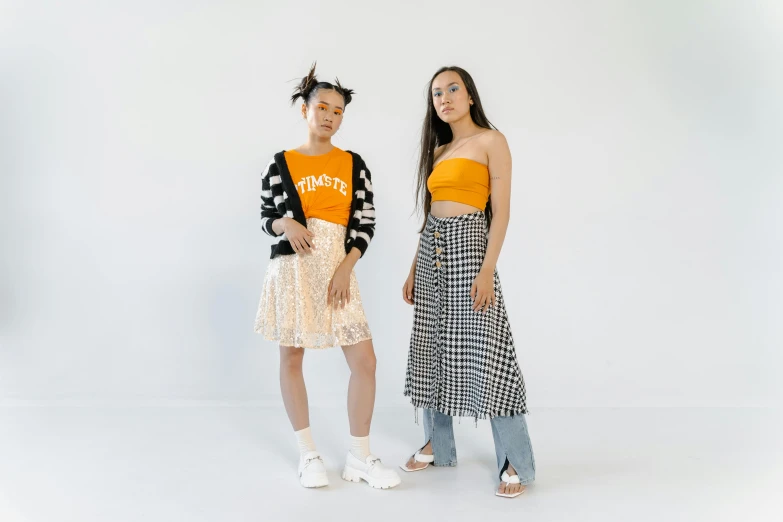 a couple of women standing next to each other, inspired by Wang Duo, trending on pexels, orange and white, wearing a skirt, pokimane, studio shot