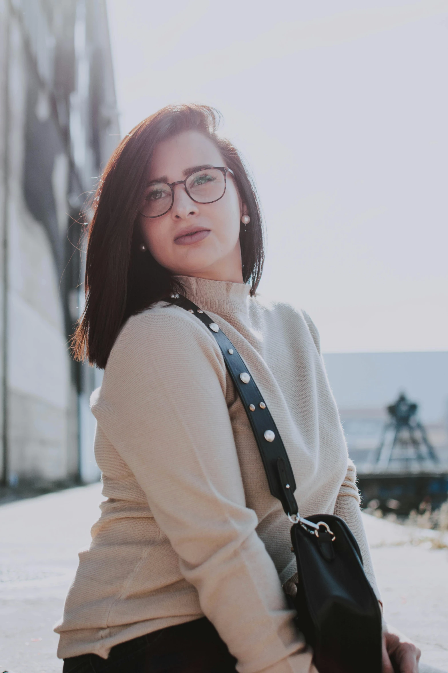 a woman sitting on the ground in front of a building, inspired by Ruth Jên, trending on pexels, in square-rimmed glasses, wearing sweater, portrait of modern darna, close up half body shot