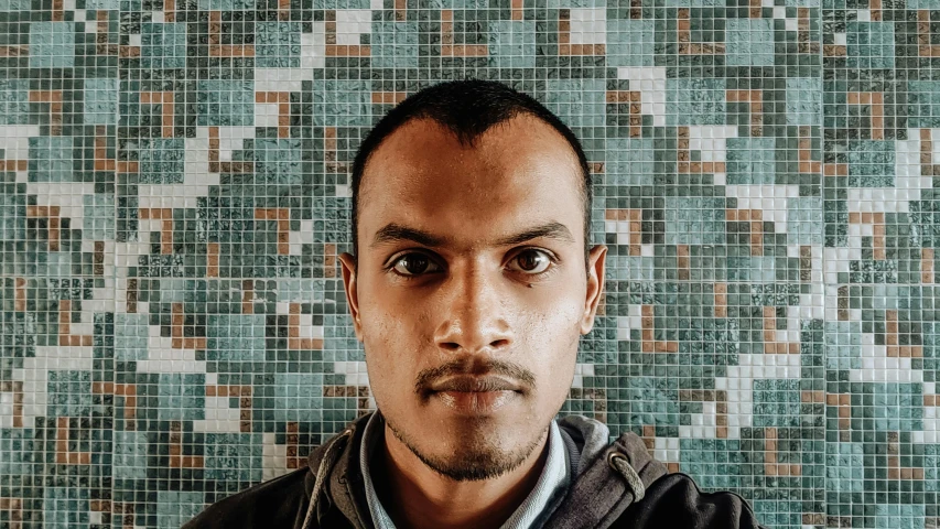 man staring ahead in front of mosaic wallpaper