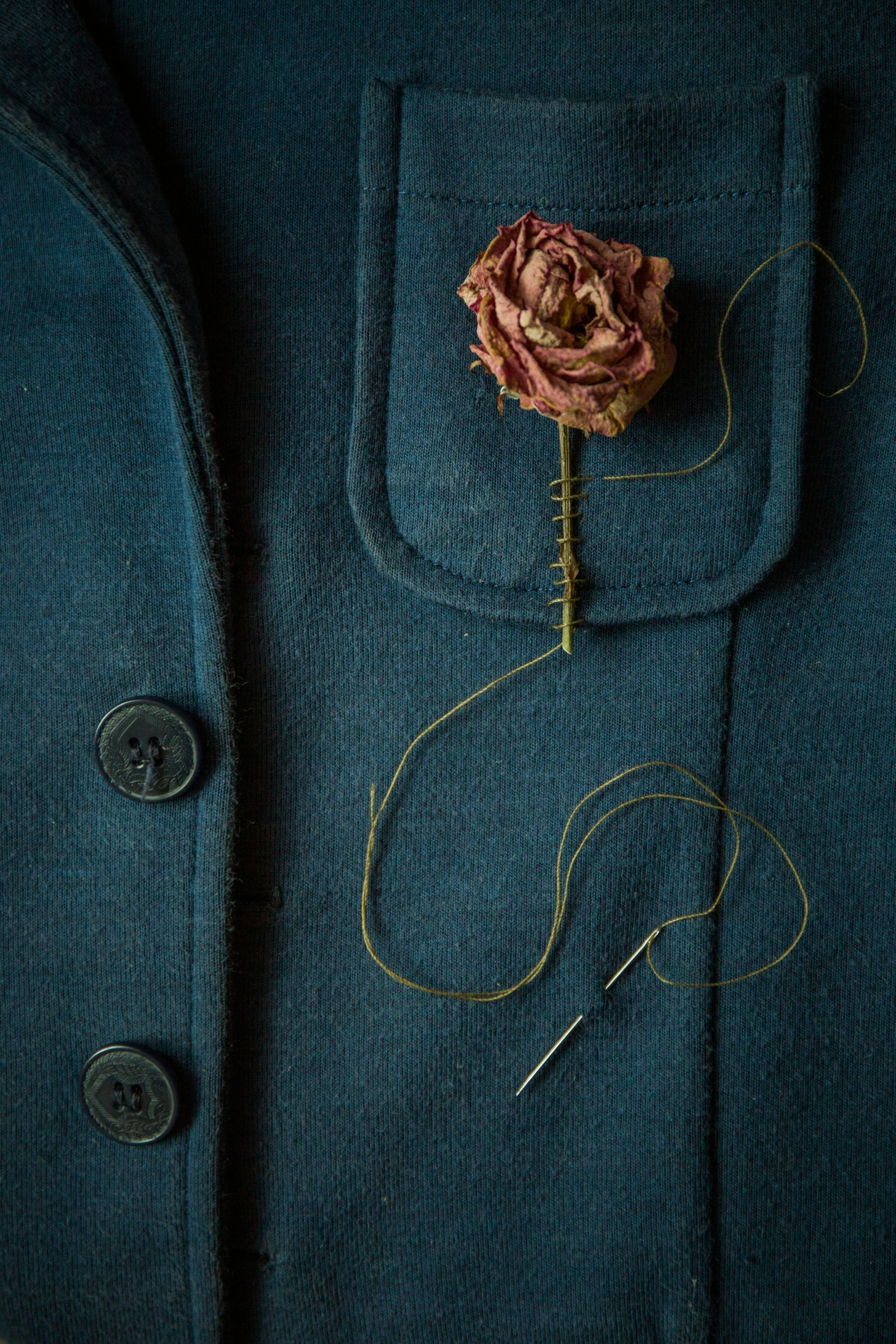 the lapel flower on a green jacket is being sewn in