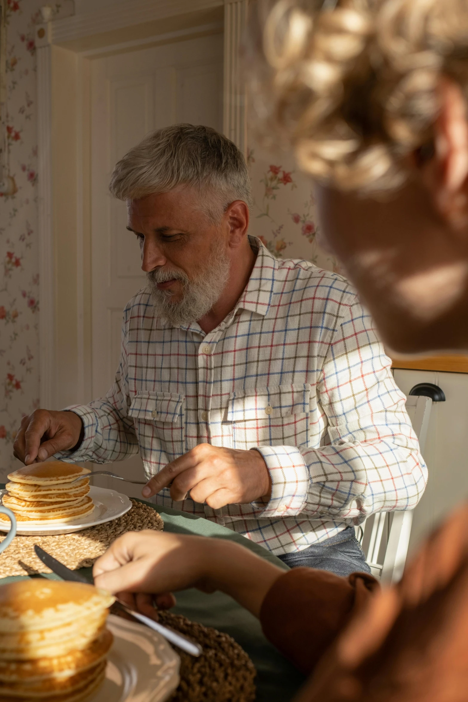 two men eating pancakes, one sitting at the table