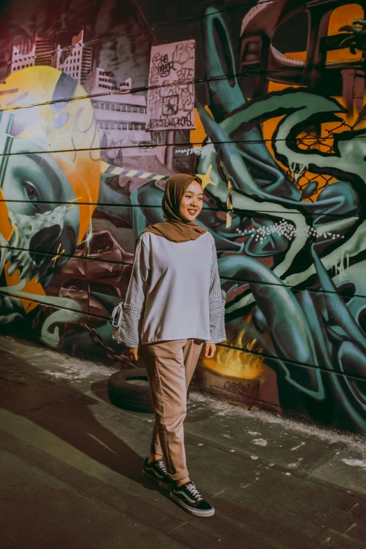 a woman standing in front of a graffiti covered wall, inspired by JoWOnder, pexels contest winner, white hijab, late evening, casual clothing style, low quality photo