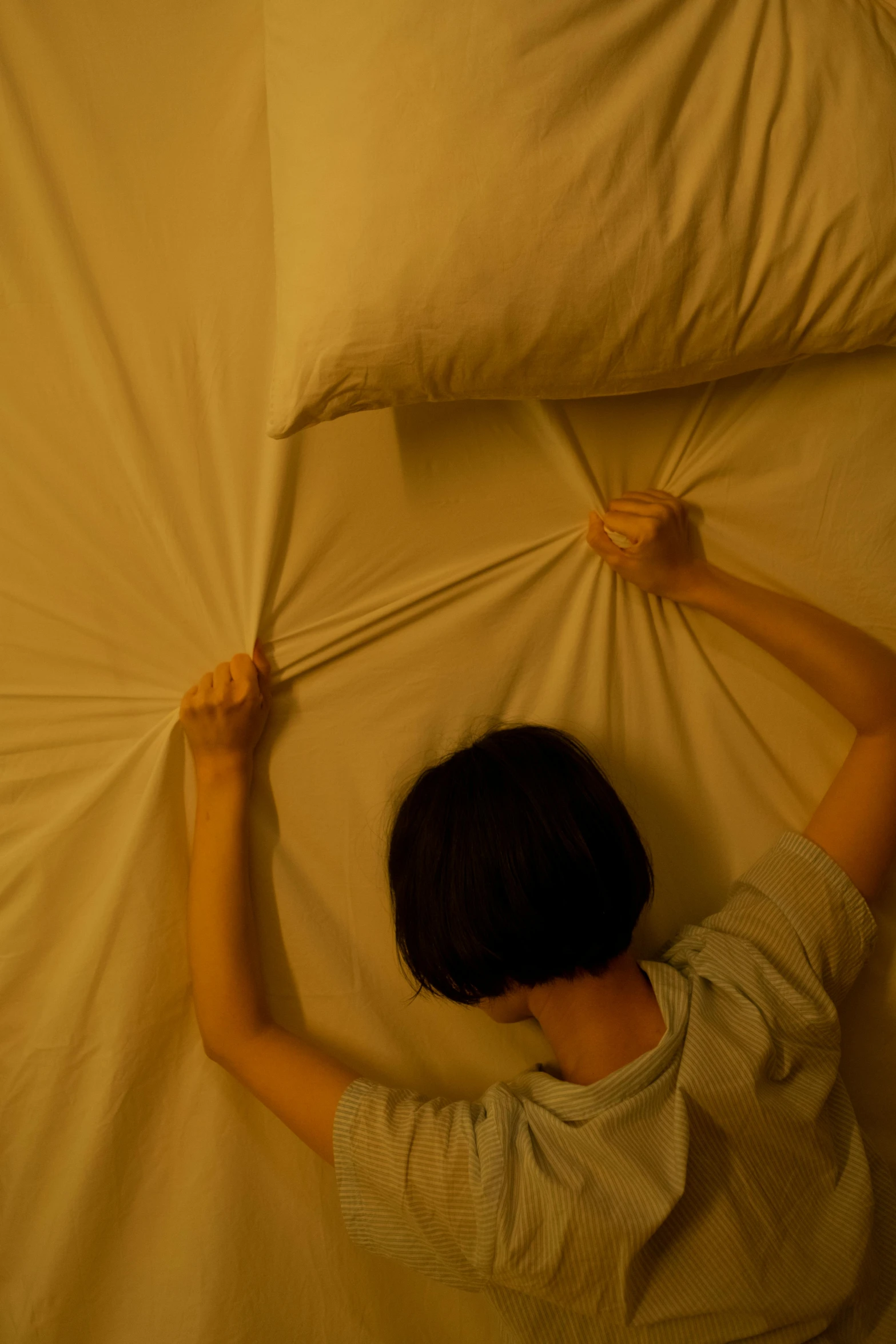 a person laying on top of a bed covered in pillows, facing away from camera, soft lighting from above, sweating, nanae kawahara