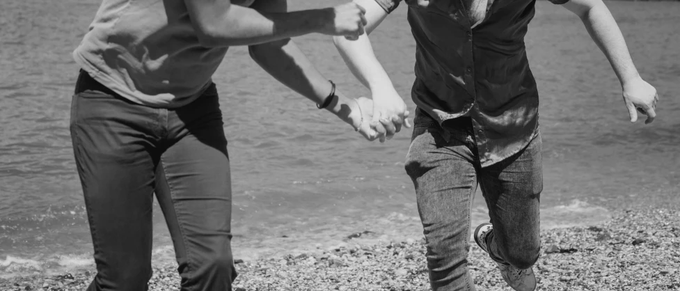 a black and white photo of two people running on a beach, a black and white photo, pexels, romanticism, holding hands, lesbians, low quality footage, close-up photo