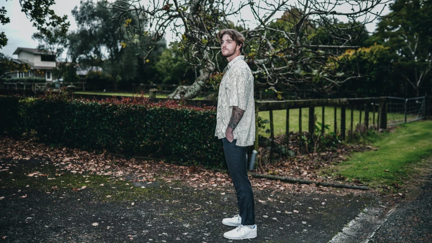 a man with tattoos stands on the pavement outside