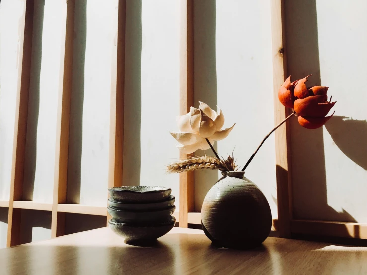 a couple of vases sitting on top of a wooden table, inspired by Itō Jakuchū, unsplash, light and space, flowers in foreground, window, various posed, hanafuda