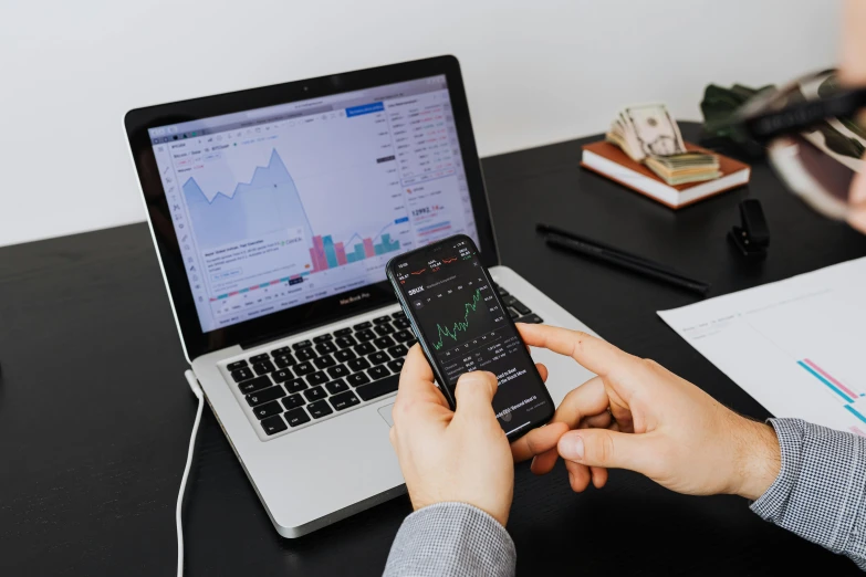 a person sitting at a desk with a laptop and a cell phone, trending on pexels, analytical art, displaying stock charts, 🦩🪐🐞👩🏻🦳, product introduction photo, maths