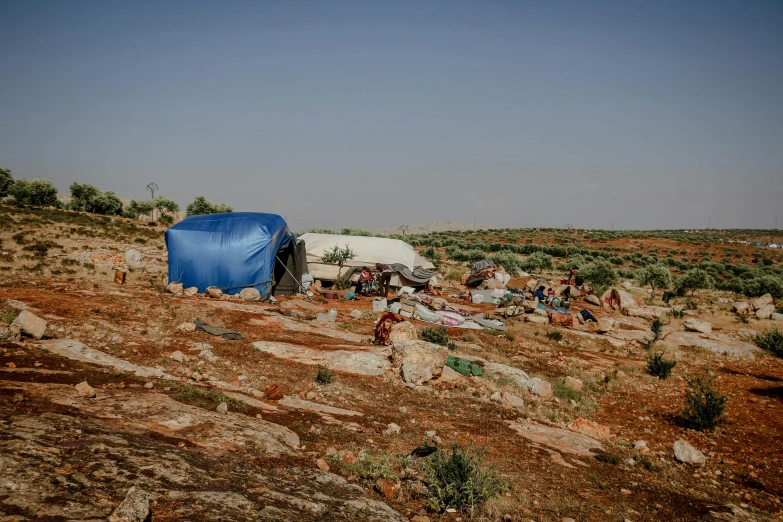 a group of people standing on top of a dirt field, by Jessie Algie, hurufiyya, tents, junk on the ground, mediterranean, profile image