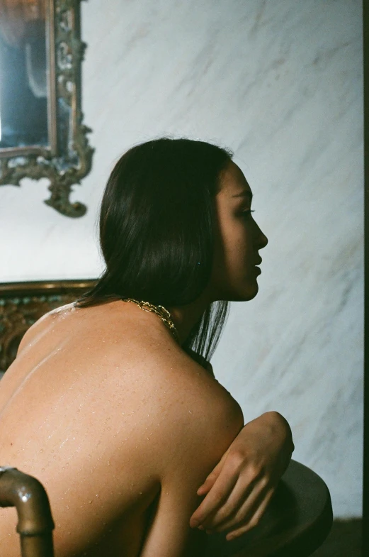 a naked woman sitting on a bed next to a mirror, an album cover, inspired by Elsa Bleda, unsplash, renaissance, young asian woman, neck chains, seen from the back, proud looking away