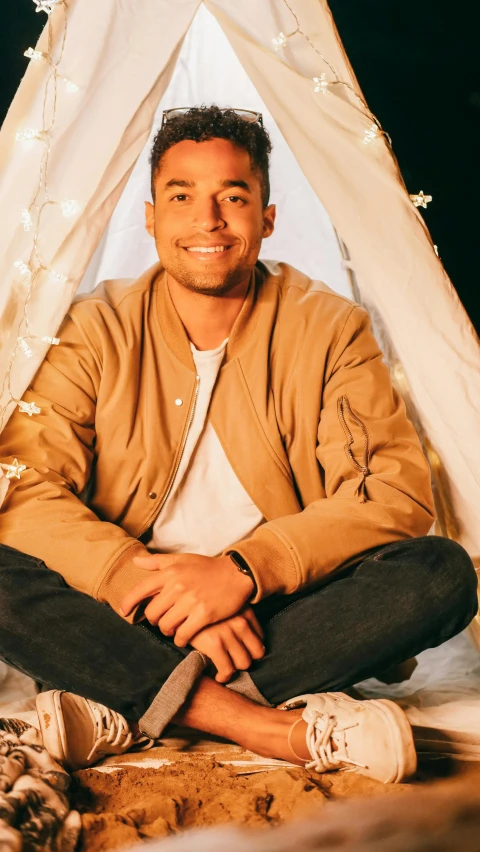 a man sitting in front of a tent next to a cat, by Robbie Trevino, smiling man, teepee, slightly tanned, vp of marketing