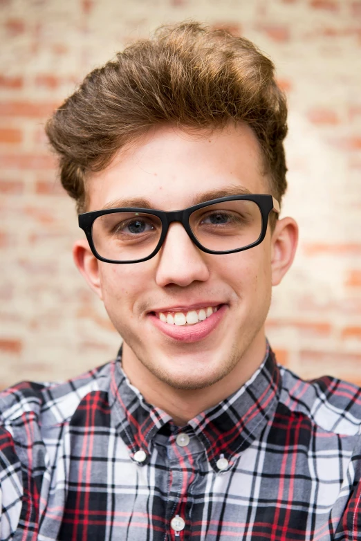 a young man wearing glasses standing in front of a brick wall, inspired by Josh Bayer, shutterstock, photorealism, smileing nright, shaven, square glasses, 1 9 year old