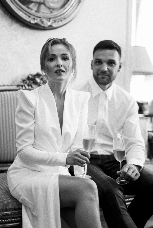 a man and a woman sitting on a couch, a black and white photo, antipodeans, champagne on the table, anastasia ovchinnikova, dressed in white, liam