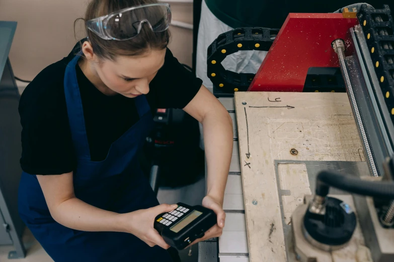 a woman working on a machine in a factory, pexels contest winner, scanning items with smartphone, wearing an apron, teenage engineering moad, avatar image