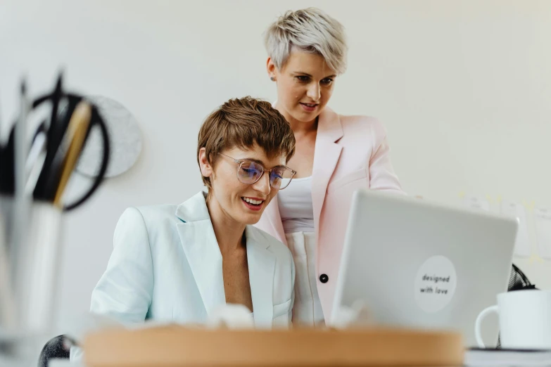 two women standing next to each other in front of a laptop, by Emma Andijewska, trending on pexels, wearing white suit and glasses, avatar image, lgbtq, unblur