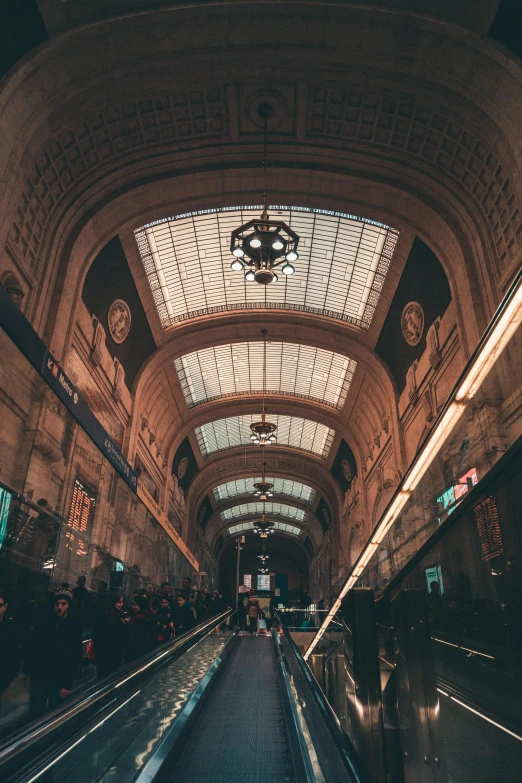 an escalator in the middle of a train station, an album cover, by Carlo Martini, unsplash contest winner, art nouveau, lights on ceiling, massive arch, bustling with people, thumbnail