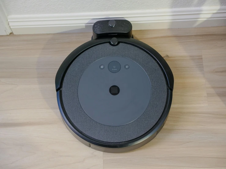 a black robot sitting on top of a wooden floor, huge black circle, top lid, vacuum, slightly pixelated