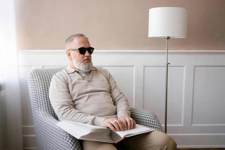 a man sitting in a chair reading a book, unsplash, hyperrealism, wearing shades, dementia, frank quitely, attractive photo