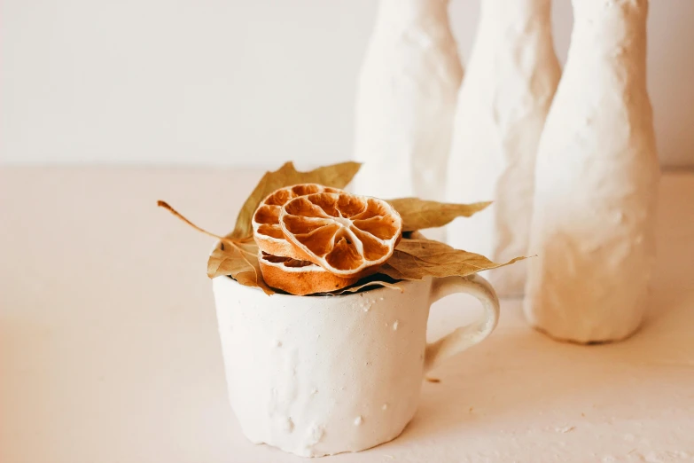 a close up of a cup with a flower in it, a still life, by Nicolette Macnamara, trending on unsplash, process art, peeled oranges, in a white boho style studio, soap carving, dried leaves