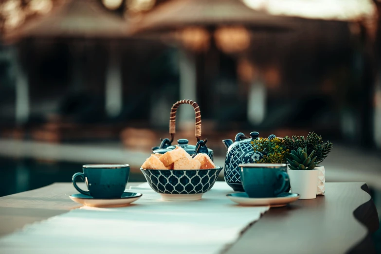 a tea pot sitting on top of a table next to two cups, inspired by Riad Beyrouti, unsplash, happening, tonal colors outdoor, teal, navy, fruits in a basket